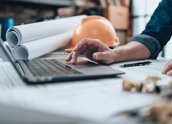 Hand using laptop with hard hat in background